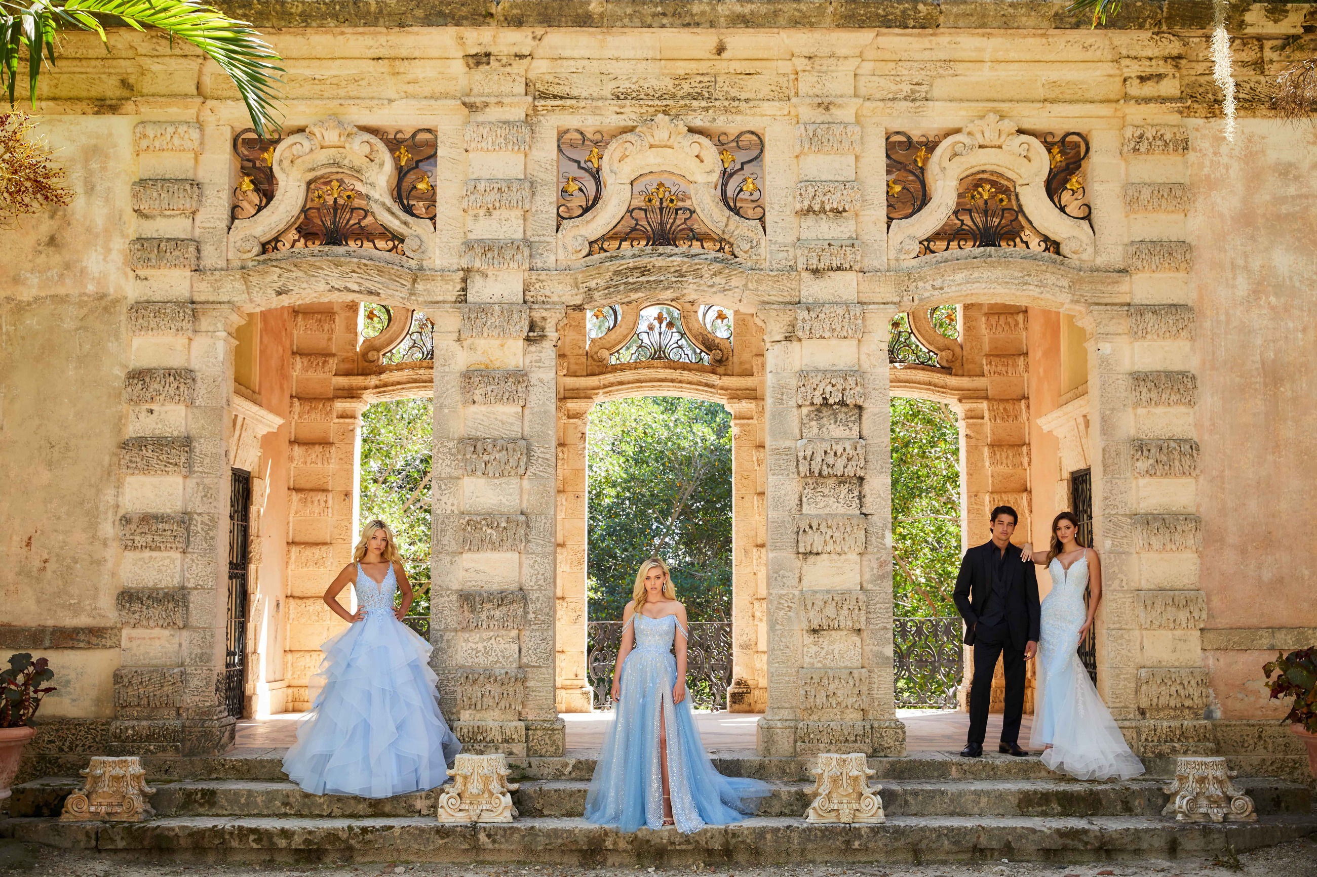 3 Girls wearing light blue dresses of different shapes in front of ancient entry. Front