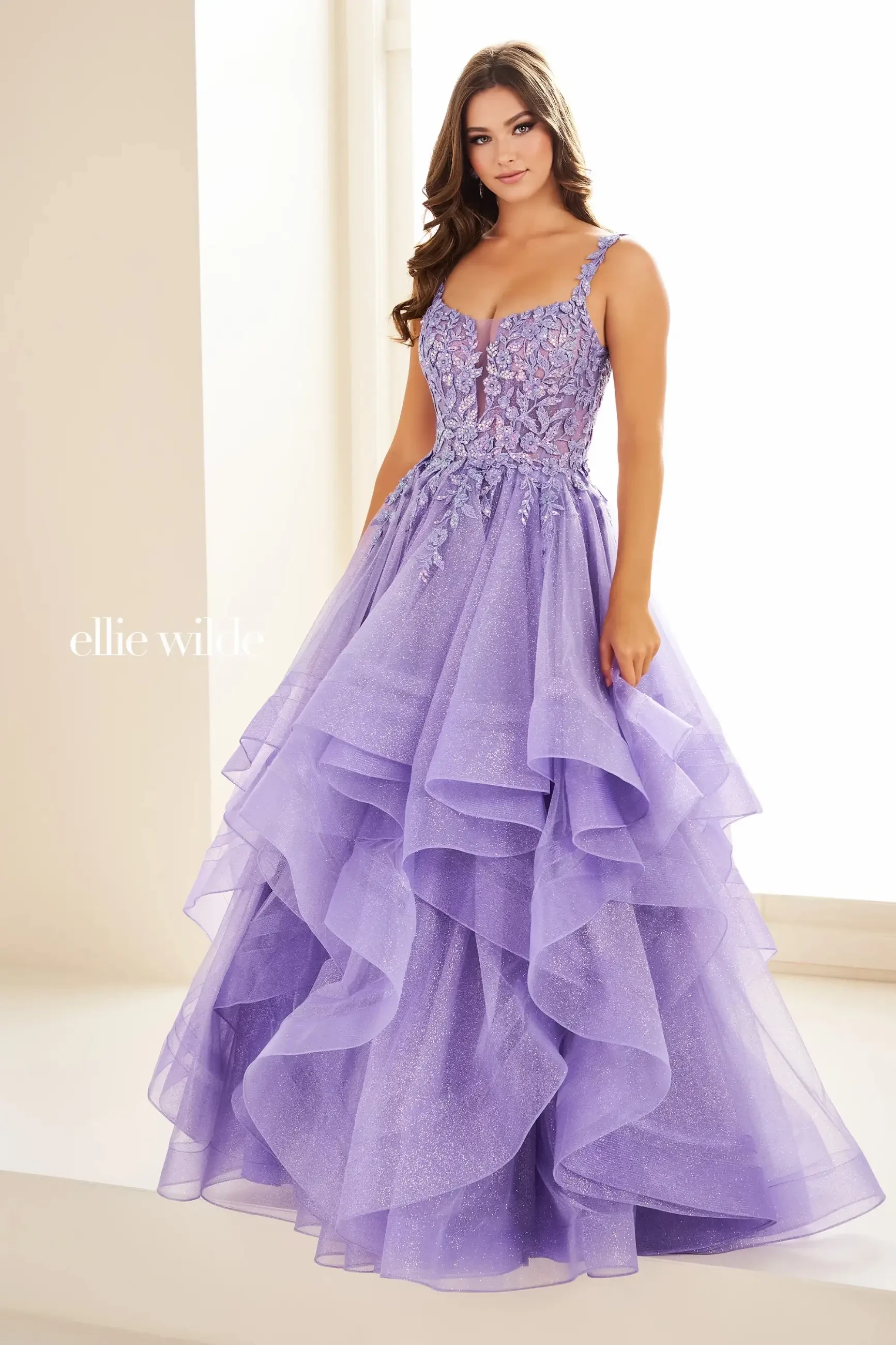Model is wearing a lavender ball gown with sequins, glitter tulle, lace appliqués, and a full skirt.