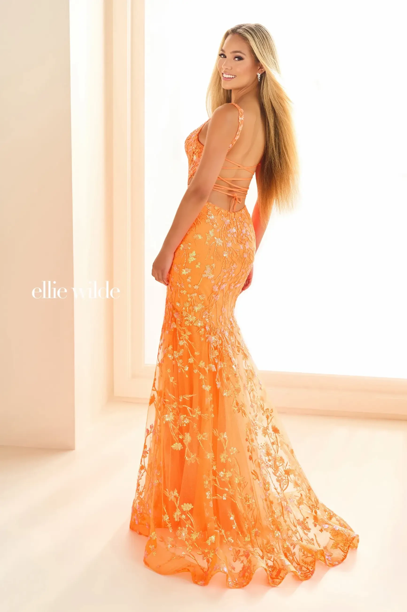Model is wearing a fiery orange mermaid gown with embroidered tulle, sequins, and a structured corset bodice.