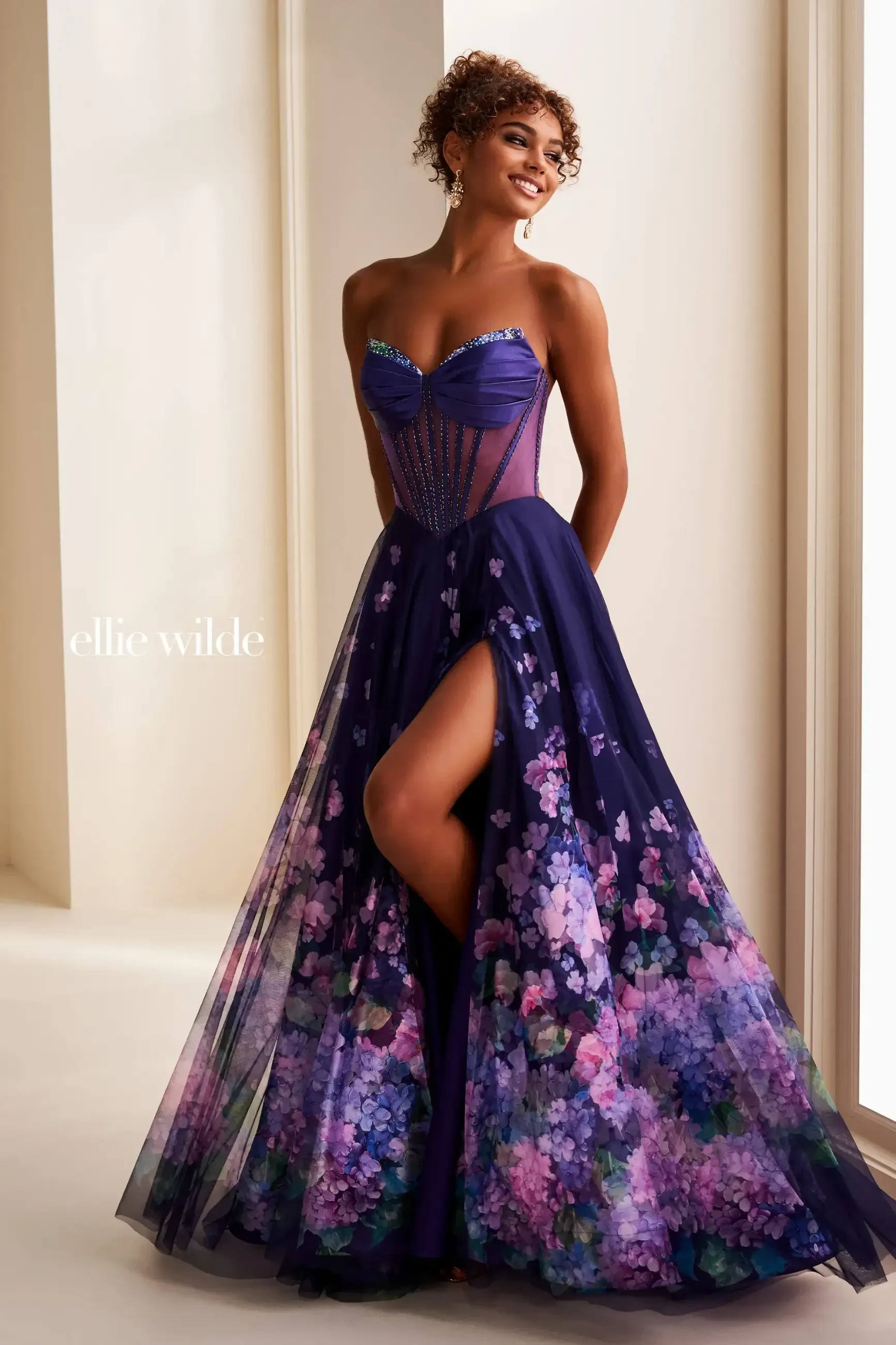 Model is wearing an a-line floral prom dress with a corset bodice and slit