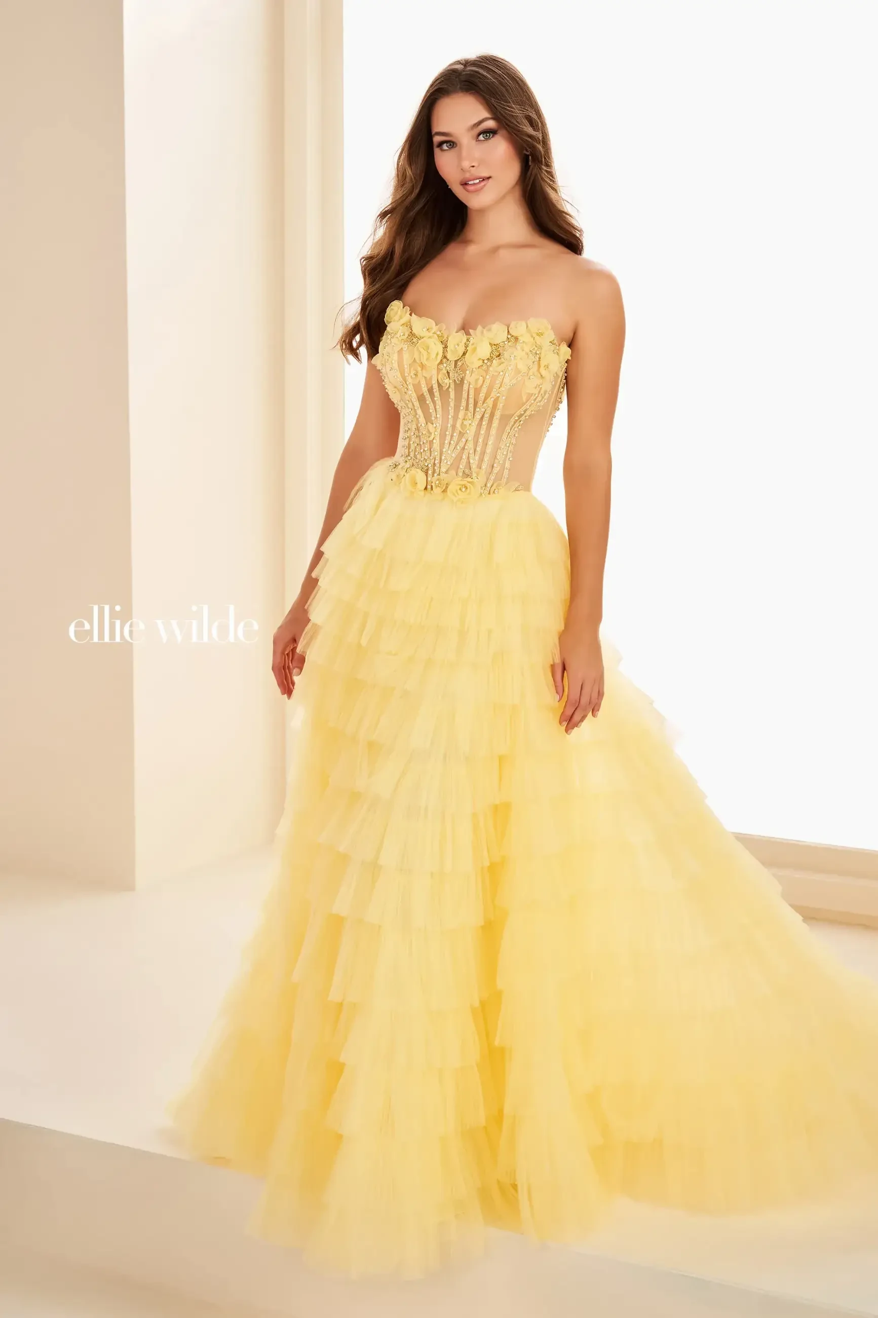 A woman in a strapless yellow gown with ruffles stands gracefully, showcasing an elegant and sophisticated look.