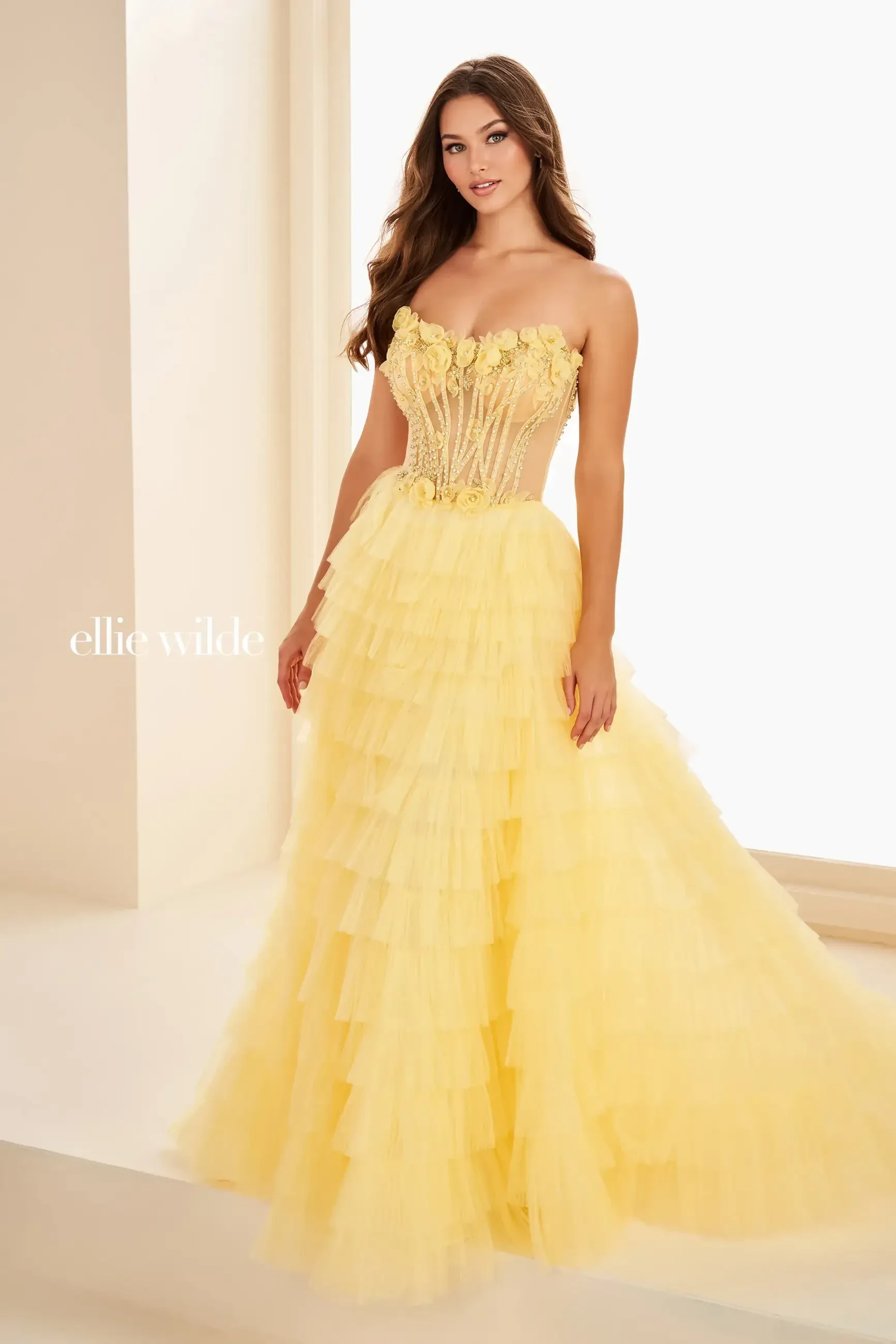 A woman in a strapless yellow gown with ruffles, standing elegantly.