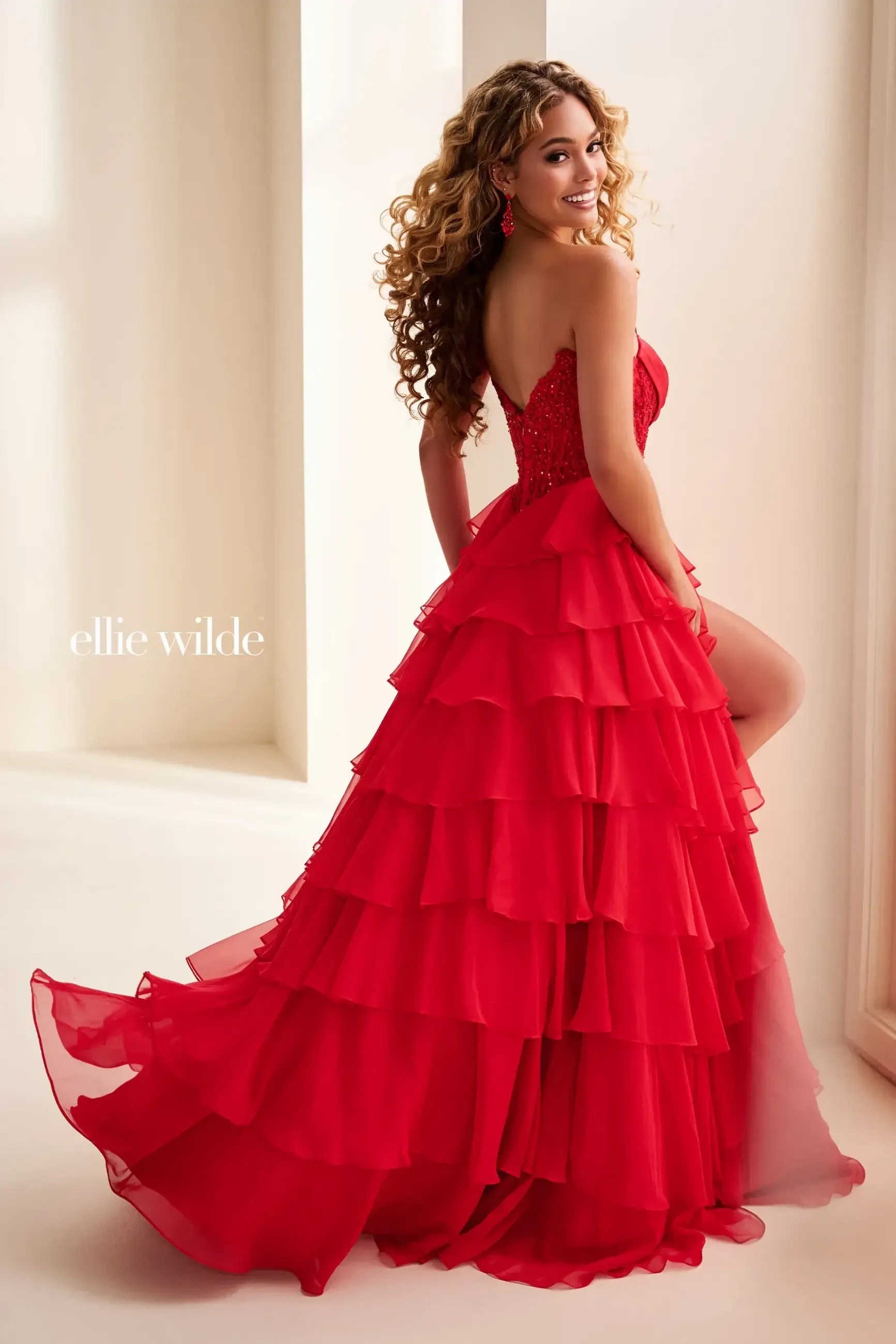 Model is wearing a red a-line prom dress with a corset bodice and layered skirt