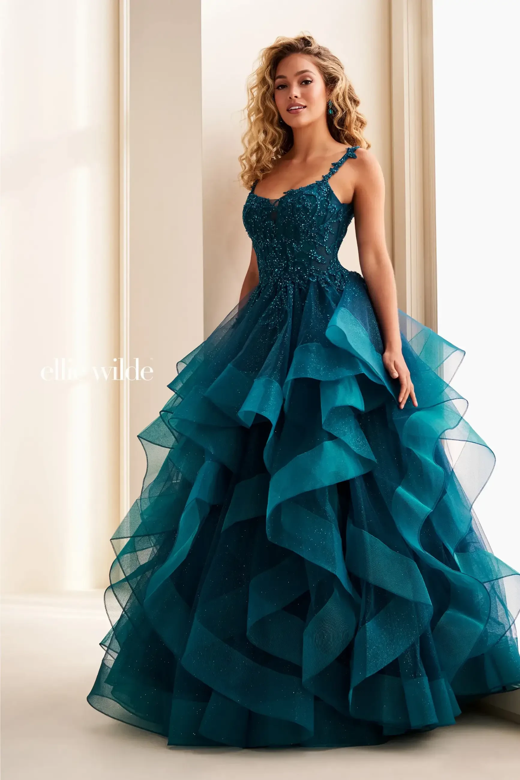Model is wearing a ball gown prom dress with lace appliques and a ruffled skirt