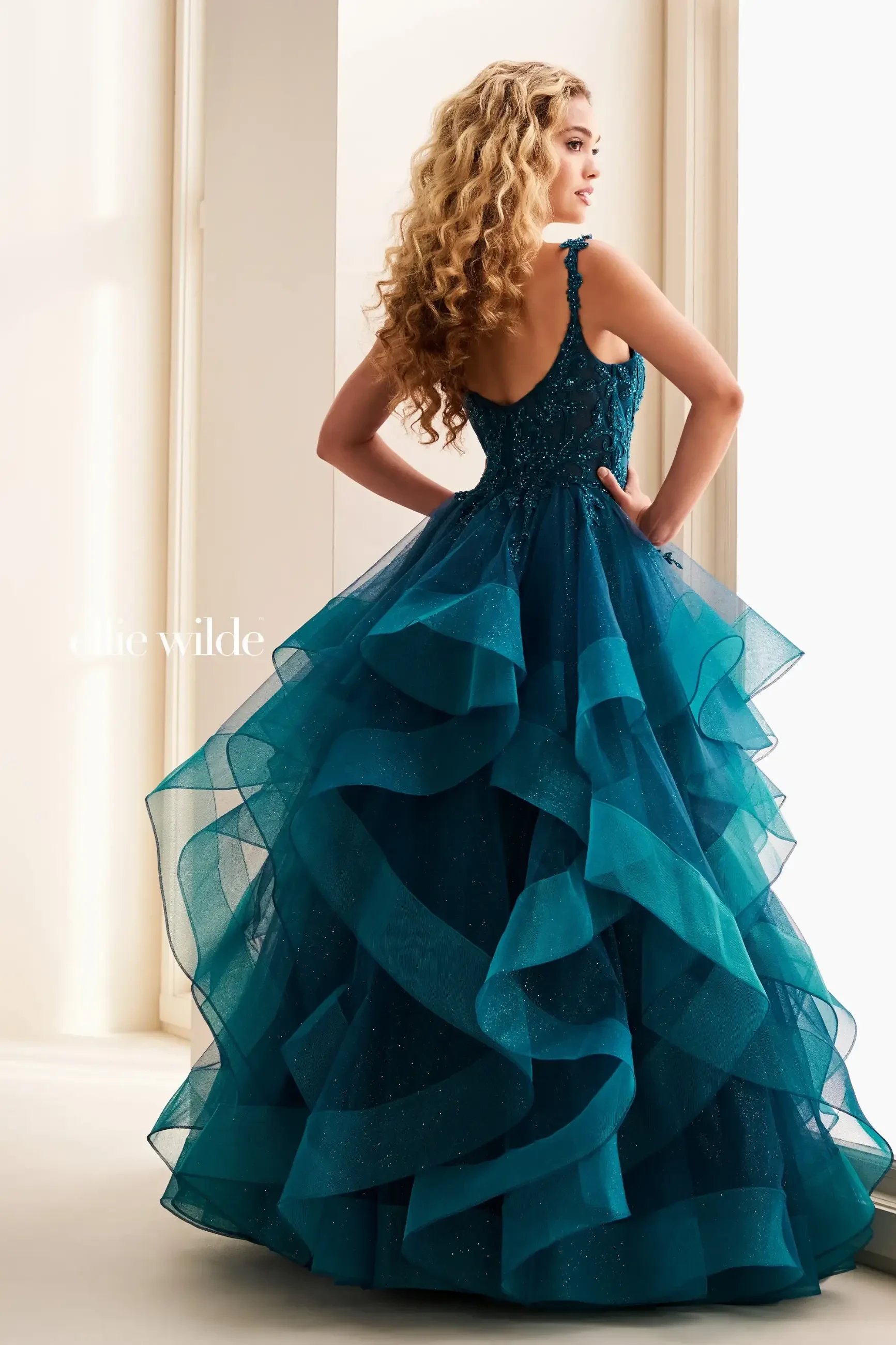 Model is wearing a ball gown prom dress with lace appliques and a ruffled skirt