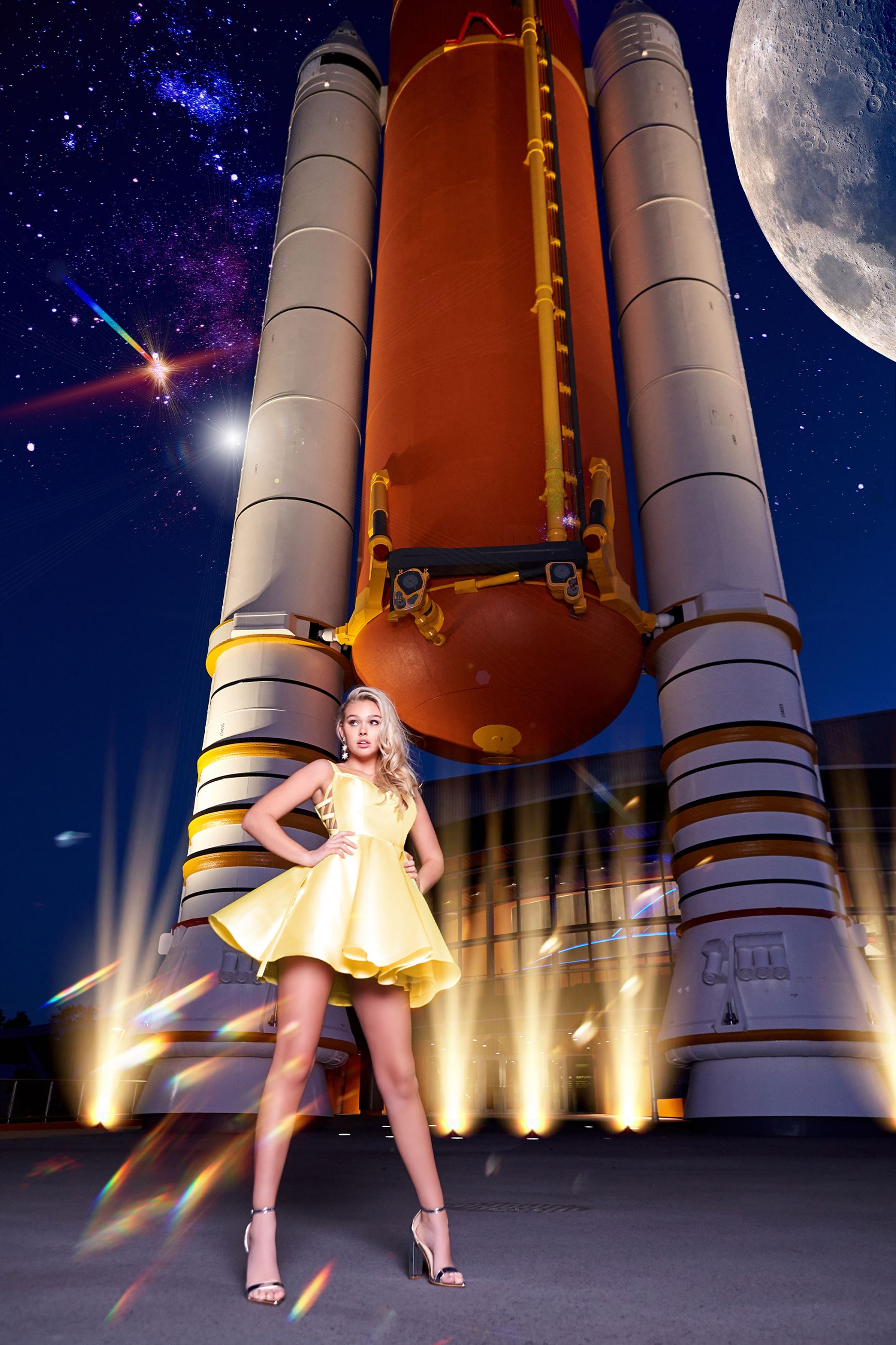 Blonde model in short yellow dress in front of rocket