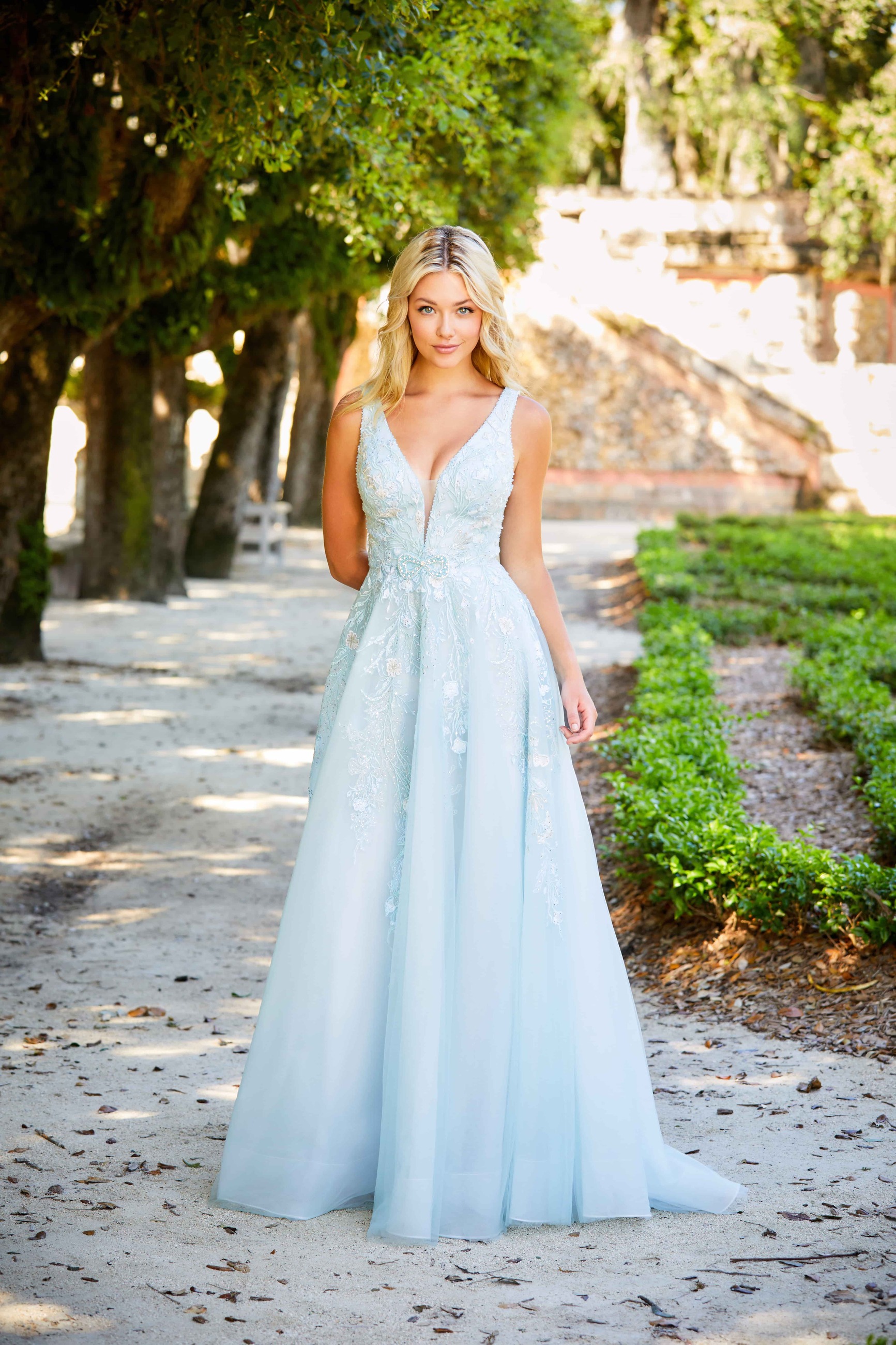 Blonde girl wearing long light blue dress near the park. Front