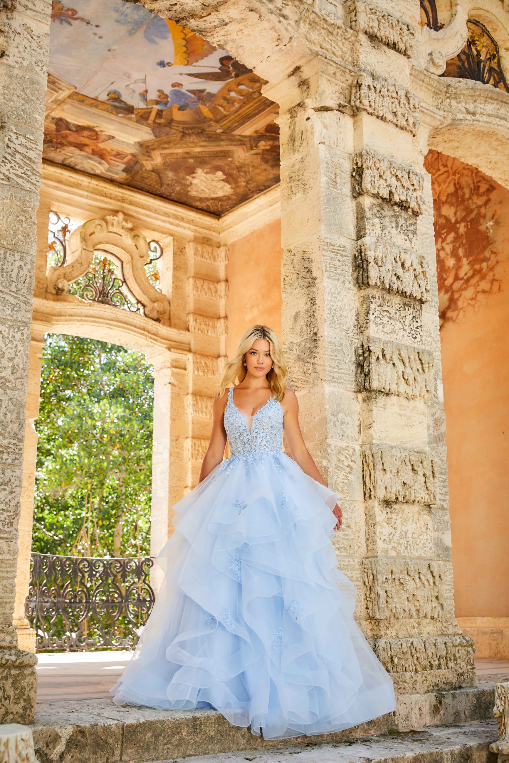 Blonde girl wearing long light blue dress near the ancient column. Front