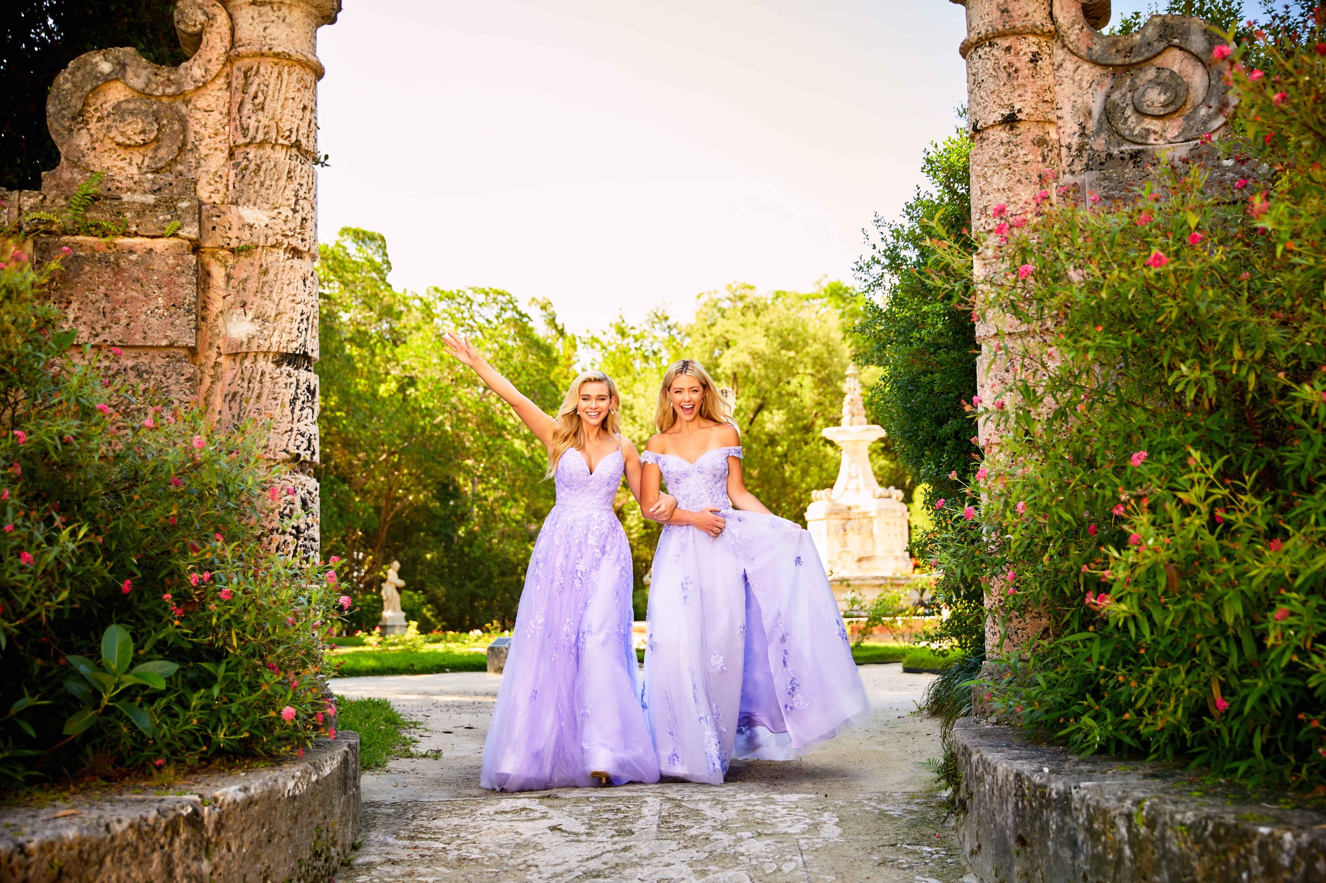 2 blonde girls wearing long blue dresses with violet shade in front of ancient arch