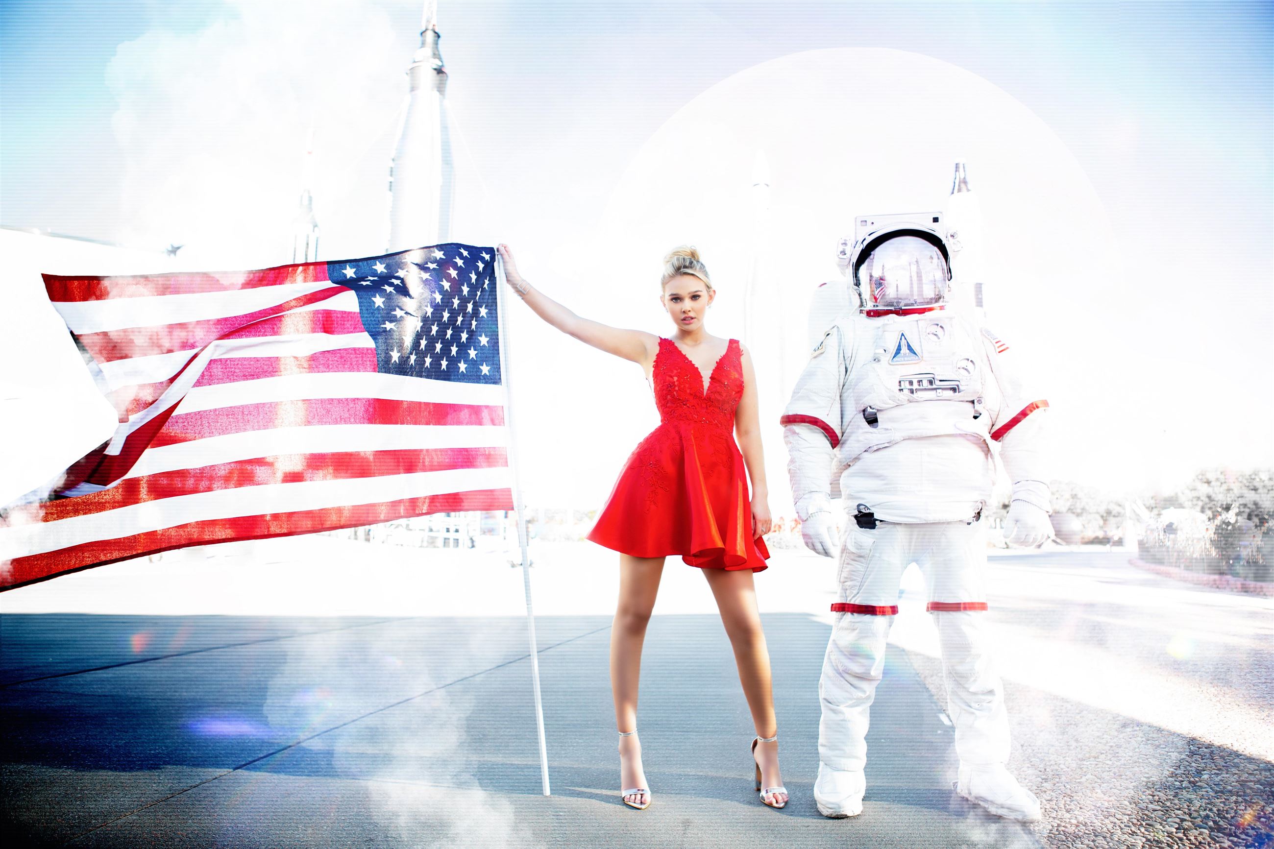 Girl next to astronaut and American flag wearing short red dress
