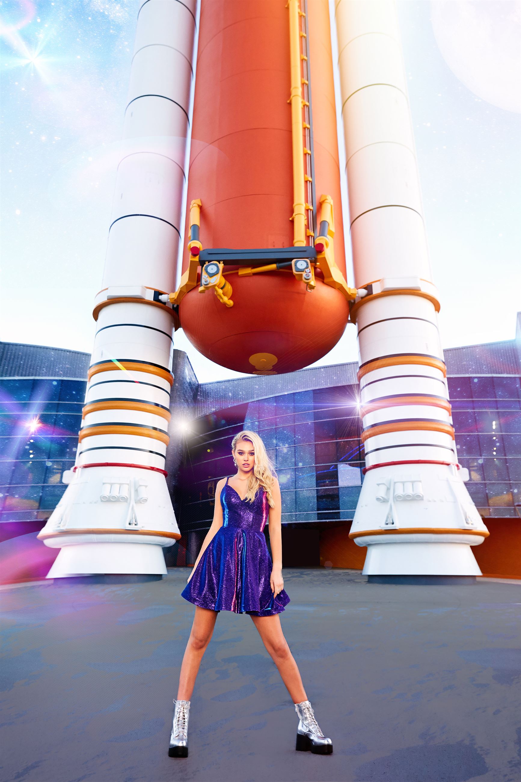 Blonde model in front of rocket wearing short purple dress